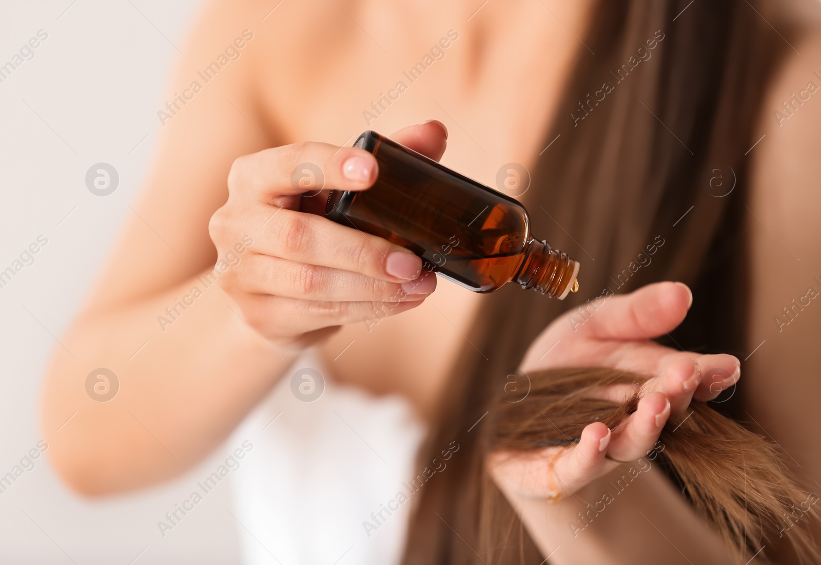 Photo of Woman applying oil onto hair against light background, closeup