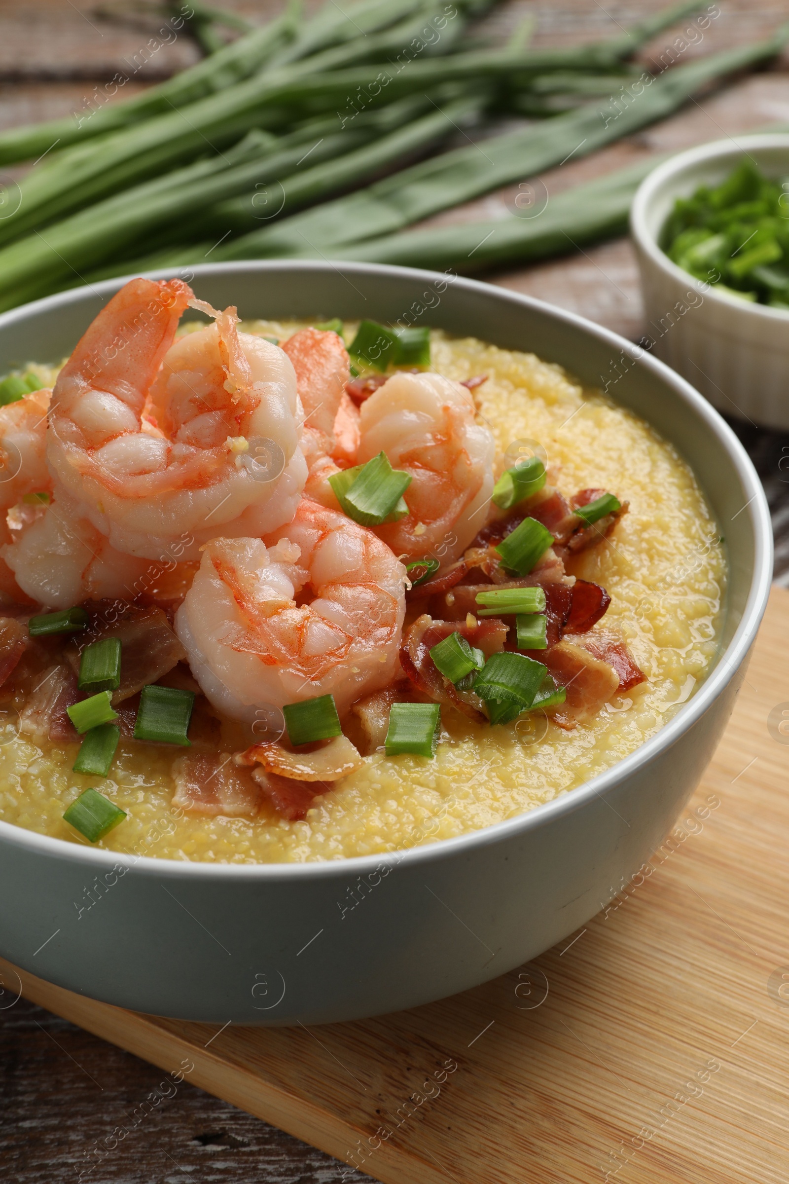 Photo of Fresh tasty shrimps, bacon, grits and green onion in bowl on table, closeup