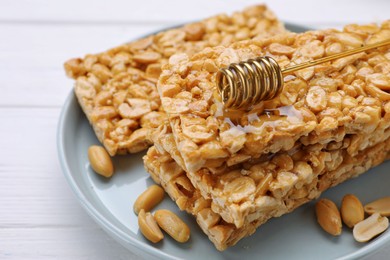 Photo of Delicious peanut bars (kozinaki) and dipper with honey on white wooden table, closeup