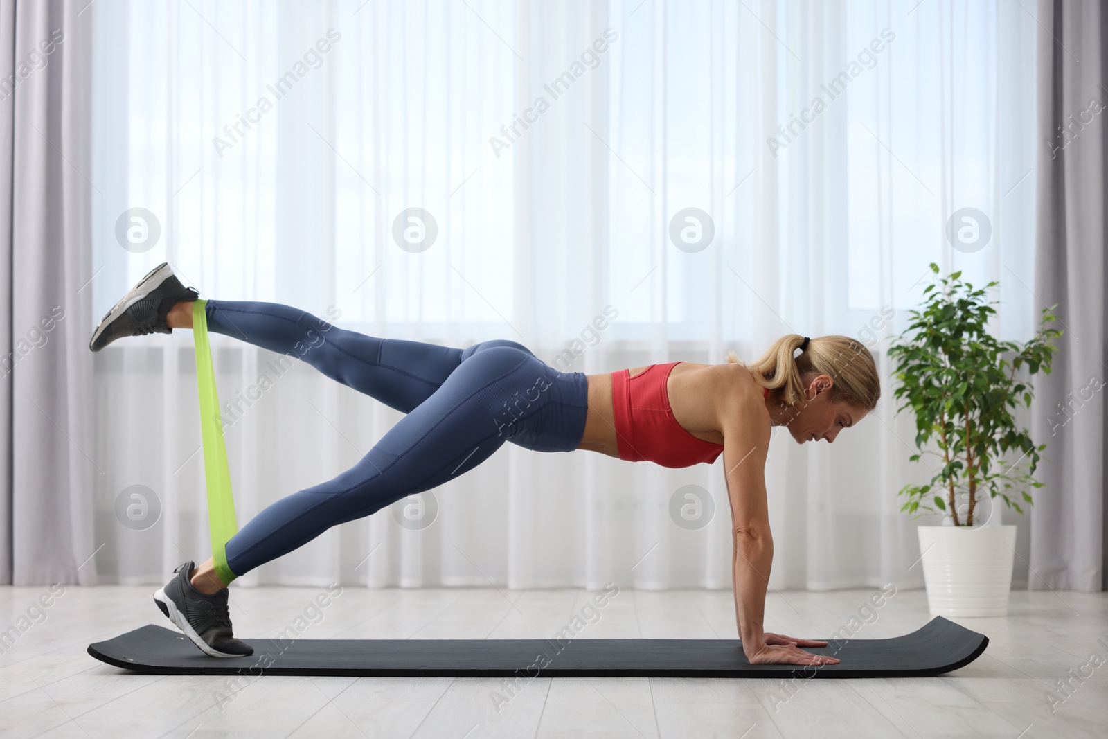 Photo of Athletic woman doing exercise with fitness elastic band on mat at home