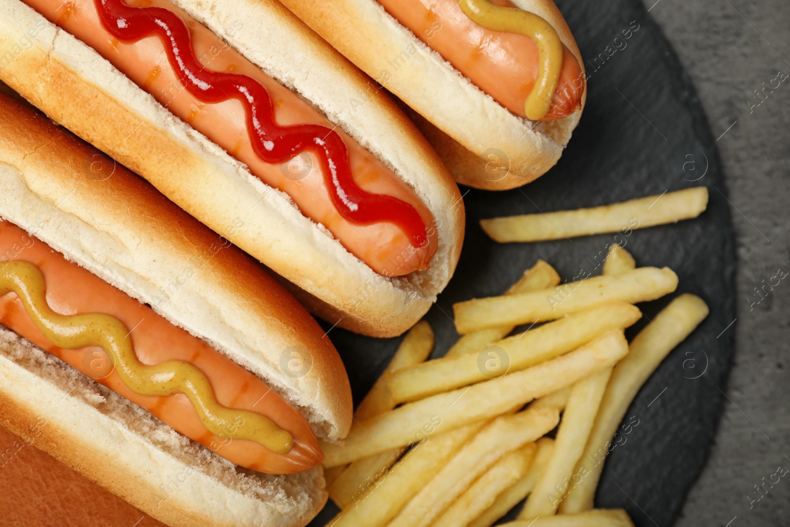 Photo of Delicious hot dogs and french fries on slate plate, top view
