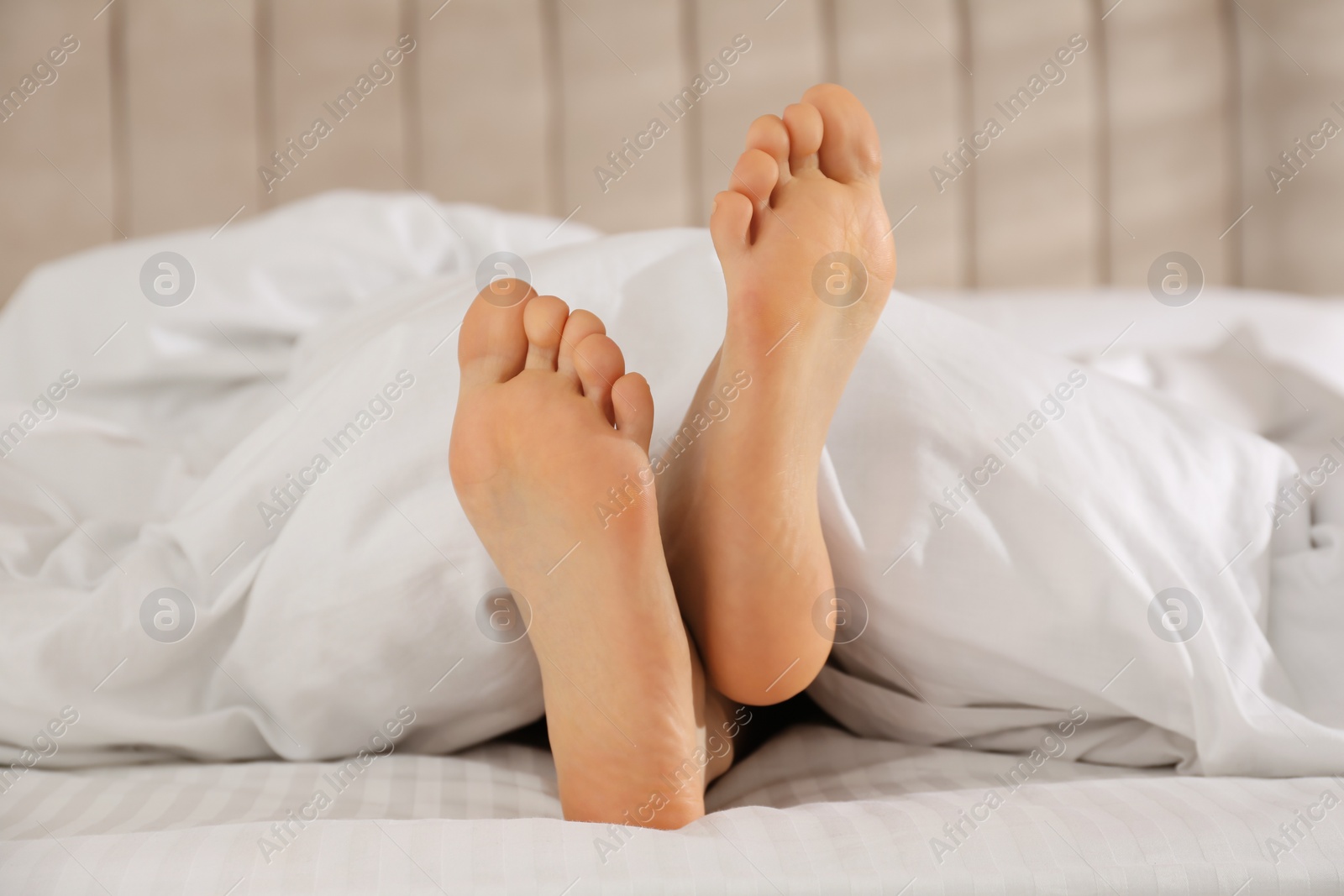Photo of Person in bed with white linens at home, closeup on feet