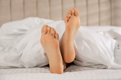 Photo of Person in bed with white linens at home, closeup on feet