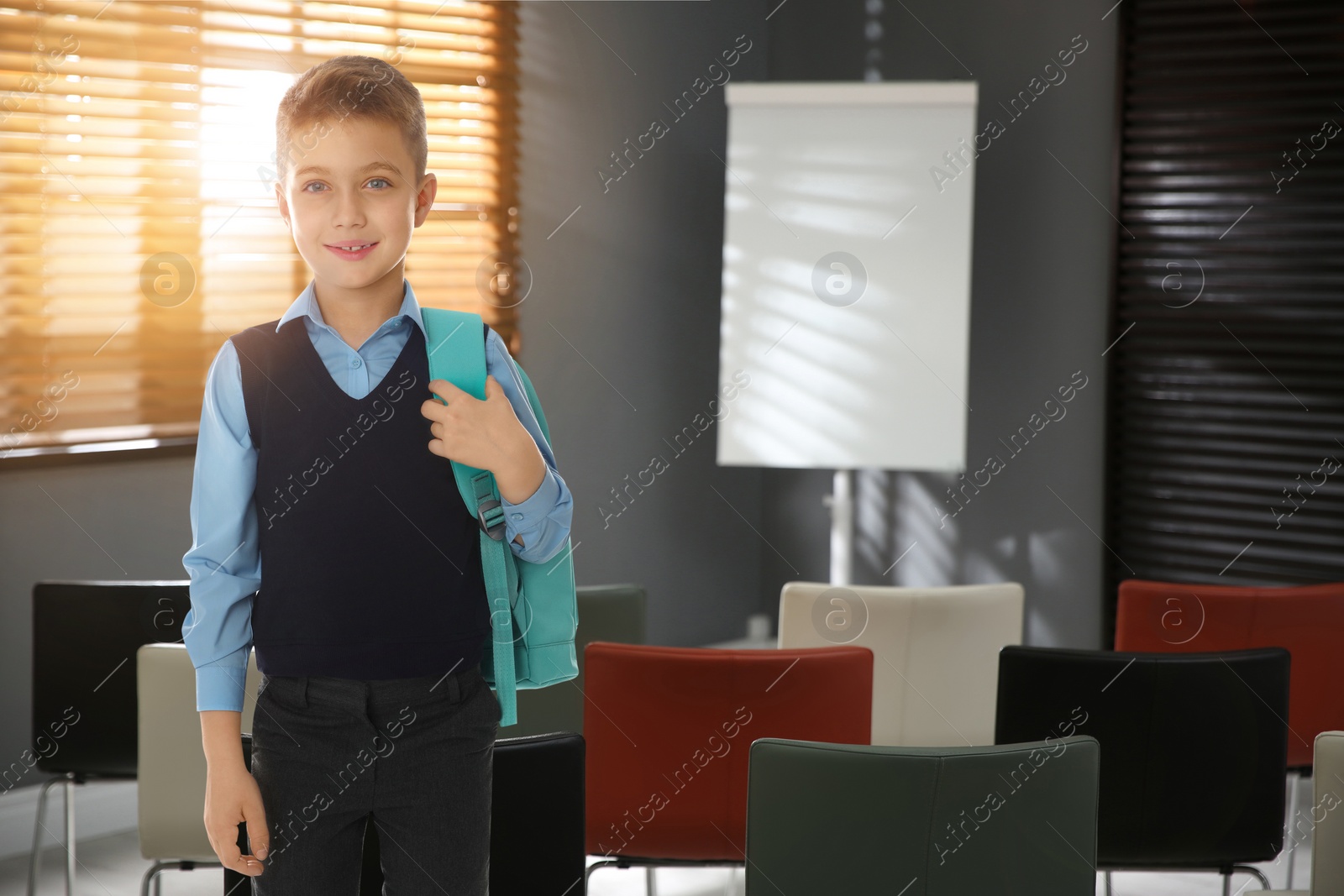 Image of Little boy with backpack in empty school classroom 