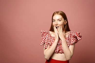 Portrait of surprised young woman on pink background, space for text
