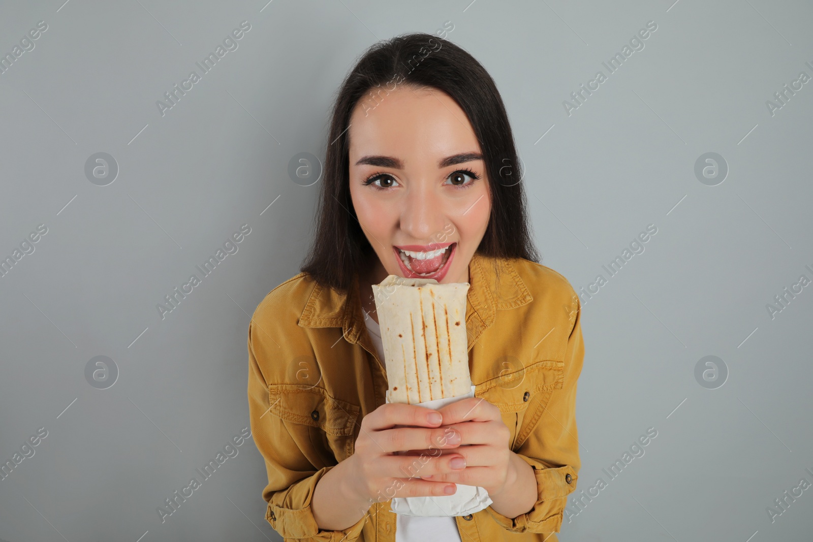 Photo of Young woman eating tasty shawarma on grey background