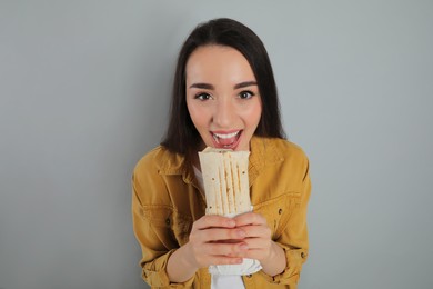 Young woman eating tasty shawarma on grey background