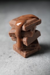 Photo of Pieces of milk chocolate with tasty paste on gray table, closeup