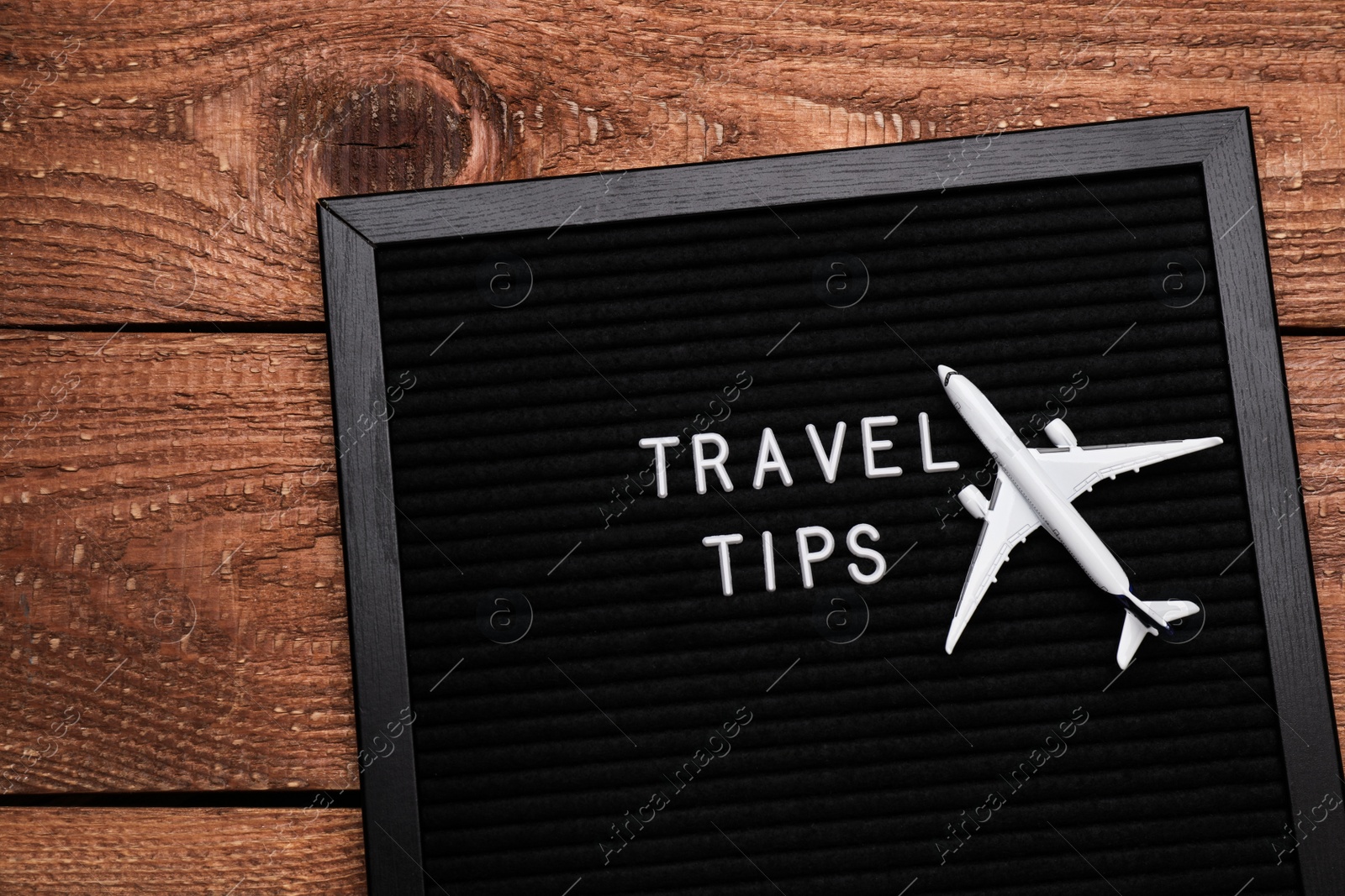 Photo of Black letter board with phrase Travel Tips and toy plane on wooden table, top view