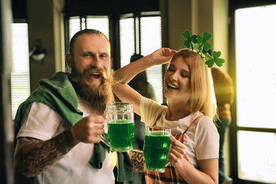 Photo of Young woman and man with glasses of green beer in pub. St. Patrick's Day celebration