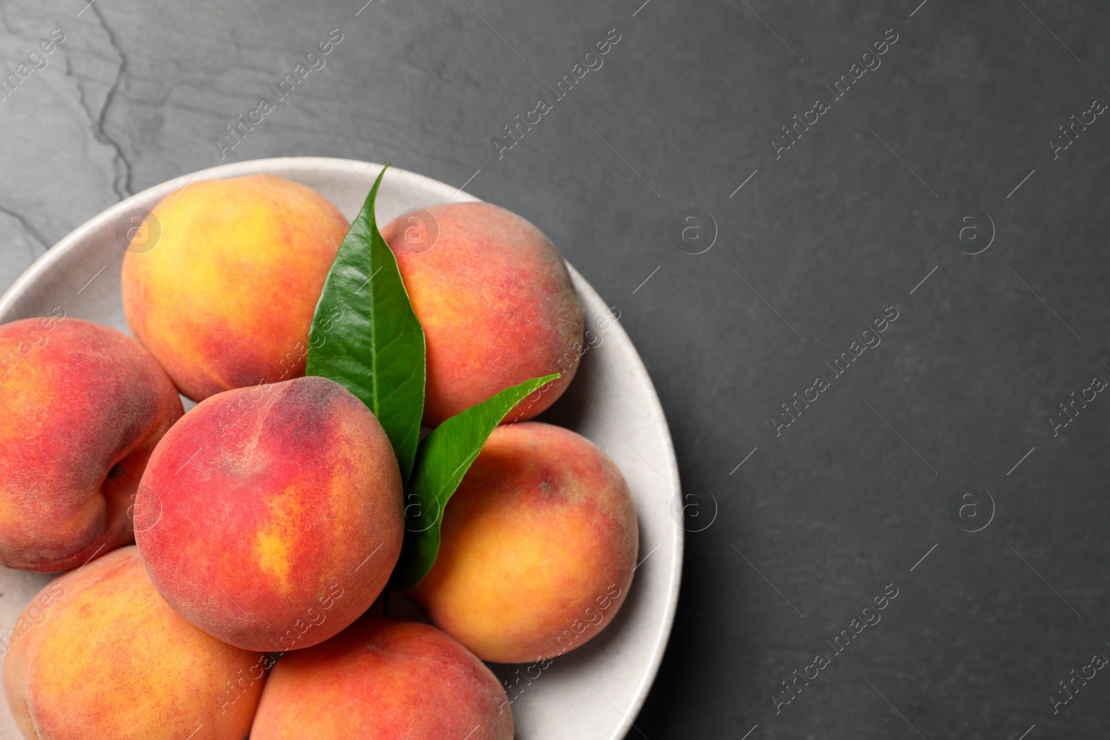 Photo of Fresh peaches and leaves in bowl on grey textured table, top view. Space for text