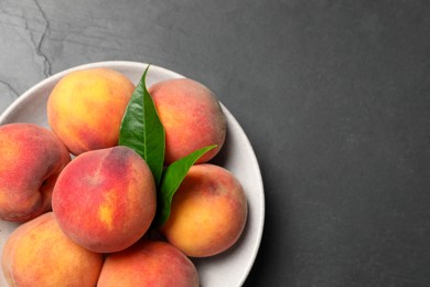 Photo of Fresh peaches and leaves in bowl on grey textured table, top view. Space for text