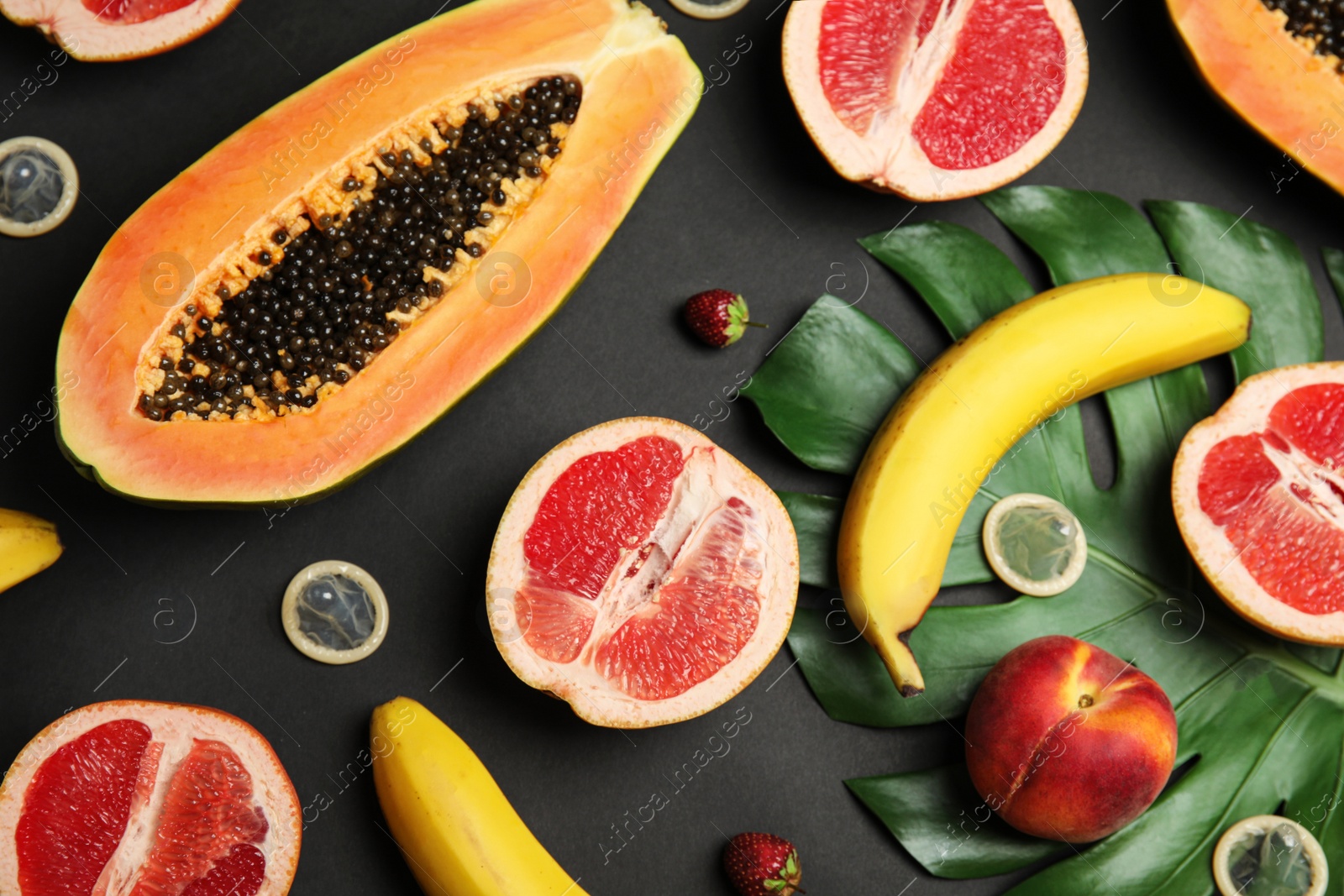 Photo of Flat lay composition with condoms and exotic fruits on black background. Erotic concept