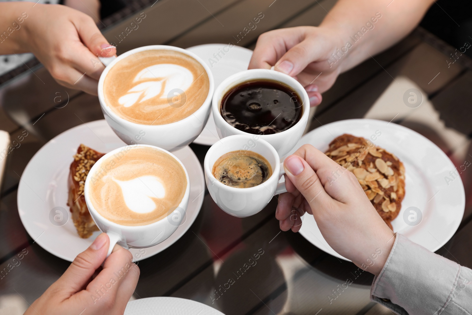 Photo of Friends drinking coffee at wooden table in outdoor cafe, closeup