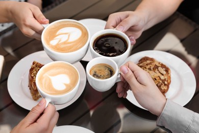 Friends drinking coffee at wooden table in outdoor cafe, closeup