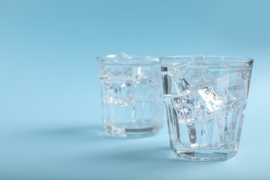 Photo of Glasses of soda water with ice on light blue background. Space for text