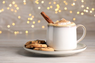 Cup of delicious eggnog with cinnamon and cookies on wooden table. Space for text