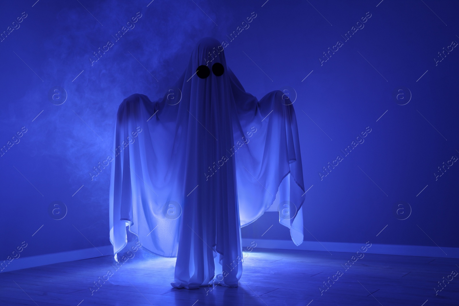 Photo of Creepy ghost. Woman covered with sheet in blue light