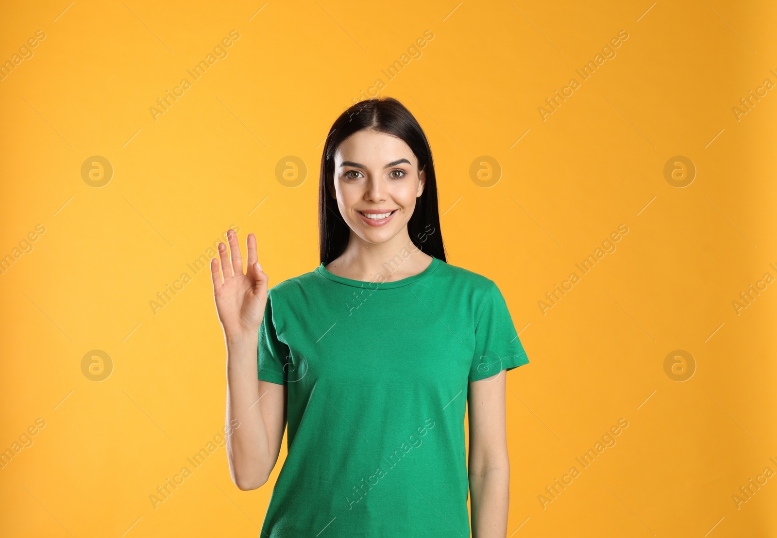 Photo of Attractive young woman showing hello gesture on yellow background