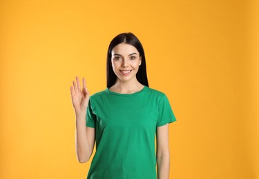 Photo of Attractive young woman showing hello gesture on yellow background