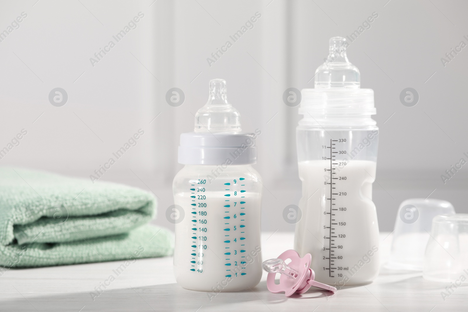 Photo of Feeding bottles with milk, pacifier and towel on white wooden table