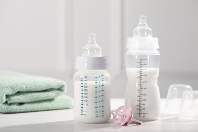 Feeding bottles with milk, pacifier and towel on white wooden table
