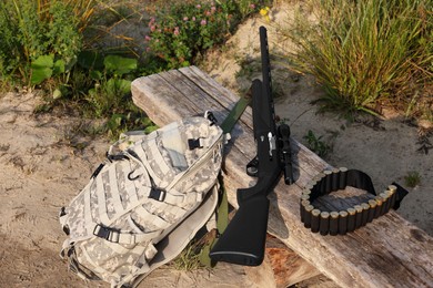 Photo of Hunting rifle, backpack and cartridges on wooden bench outdoors