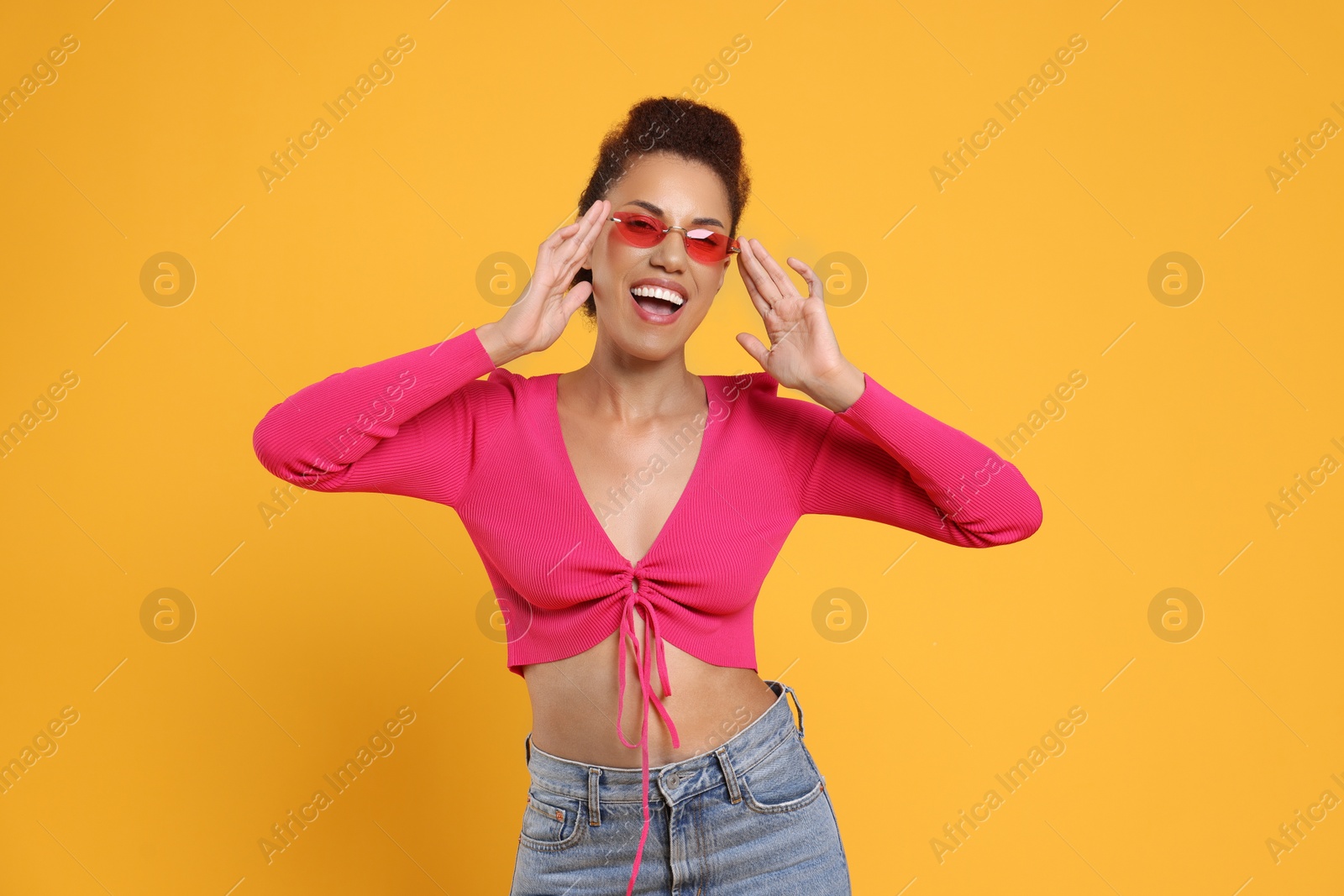 Photo of Happy young woman in stylish sunglasses dancing on orange background