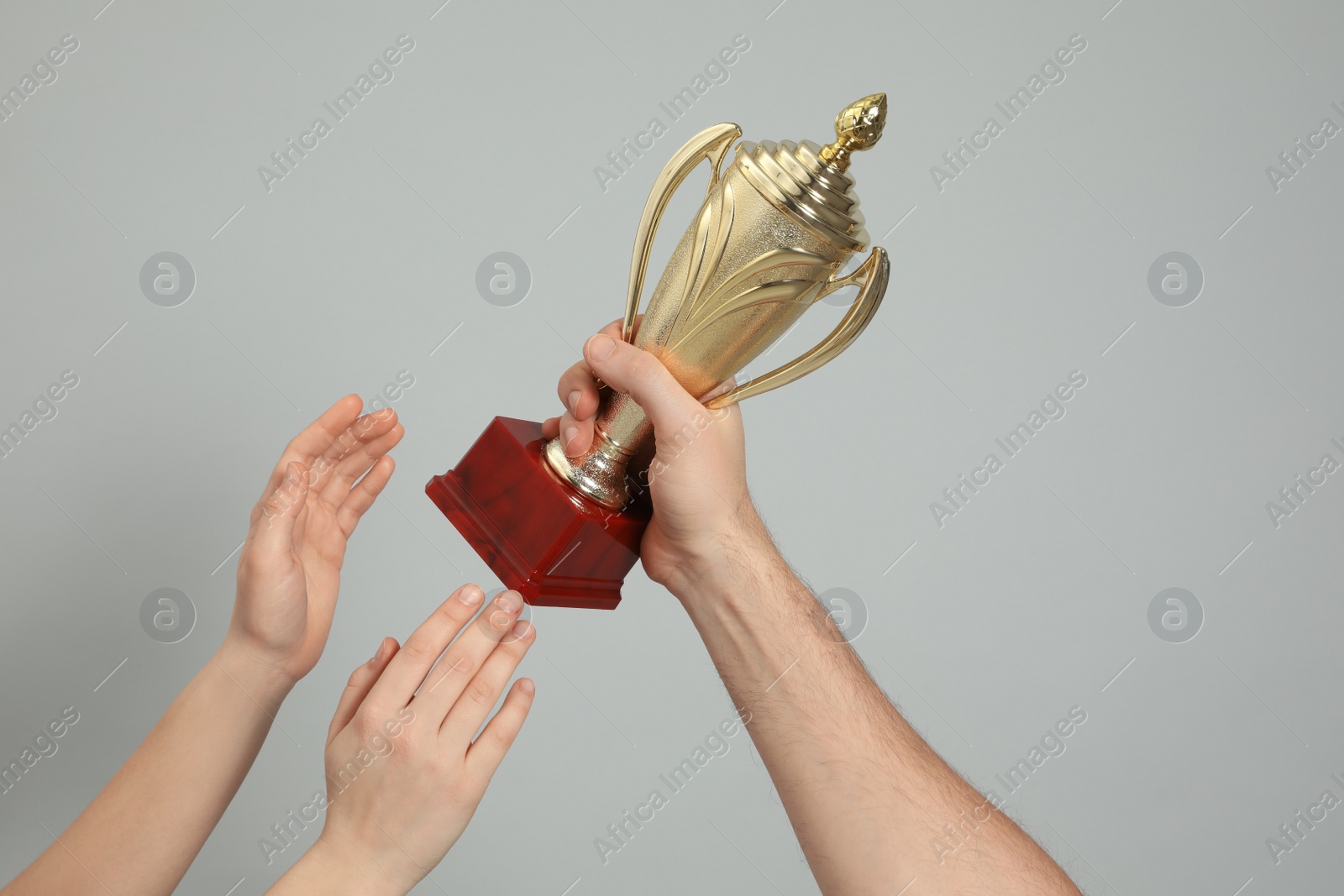Photo of People with gold trophy cup on light grey background, closeup