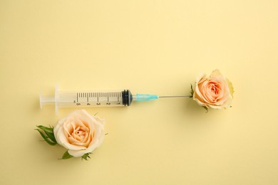 Medical syringe and beautiful roses on pale yellow background, flat lay