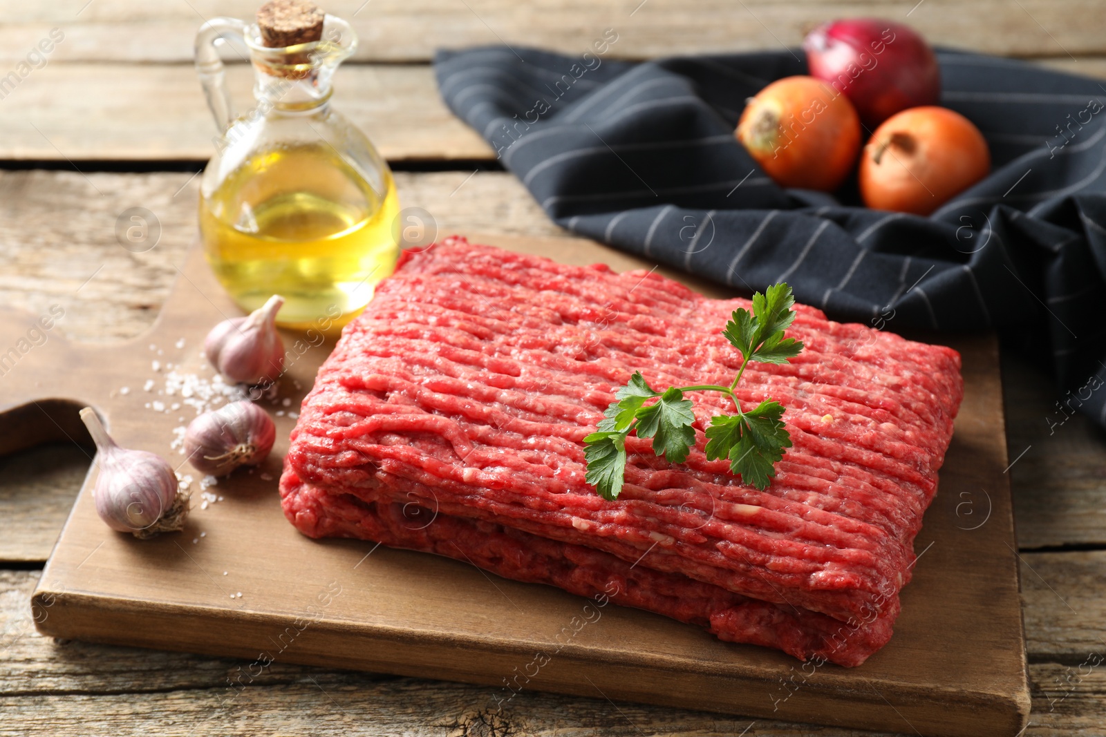 Photo of Raw ground meat, onion, garlic and oil on wooden table