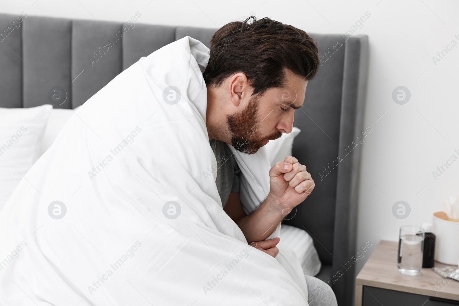 Photo of Sick man coughing on bed at home. Cold symptoms