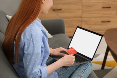 Woman with credit card using laptop for online shopping on sofa at home, closeup