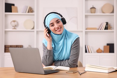 Photo of Muslim woman in hijab using laptop at wooden table in room