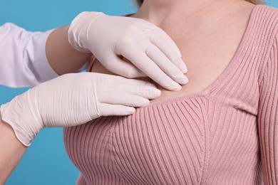 Photo of Mammologist checking woman's breast on light blue background, closeup
