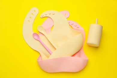 Photo of Baby feeding accessories and bibs on yellow background, flat lay
