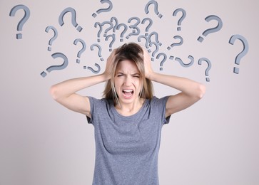 Image of Amnesia. Stressed young woman and question marks on light background