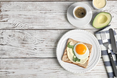 Slice of bread with fried egg, spread and arugula on white wooden table, flat lay. Space for text