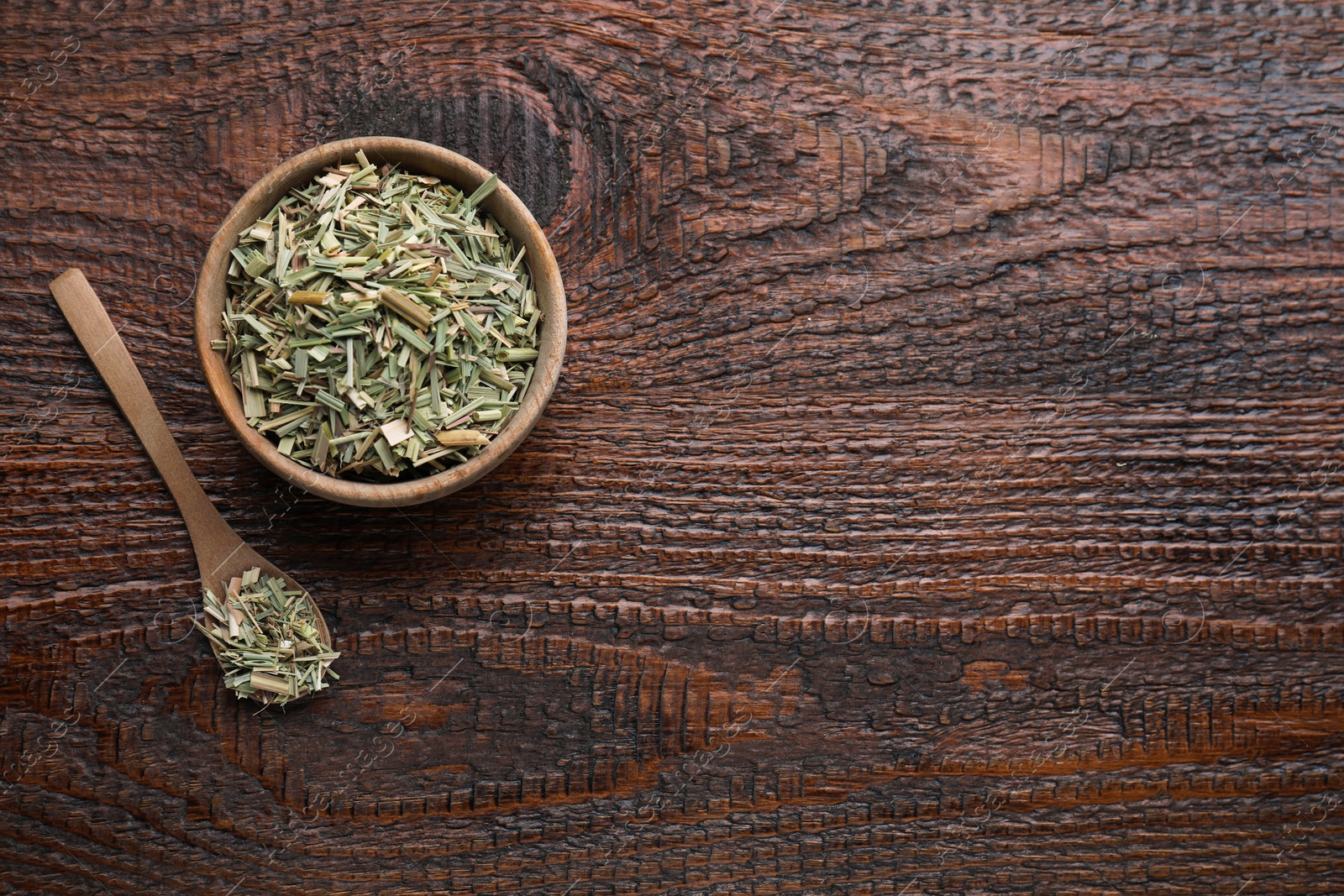 Photo of Bowl and spoon with aromatic dried lemongrass on wooden table, flat lay. Space for text