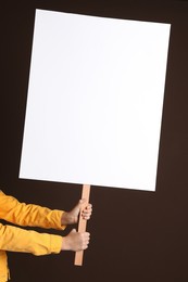 Woman holding blank sign on brown background, closeup. Space for design