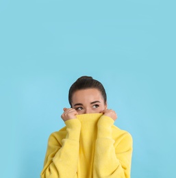 Beautiful young woman wearing yellow warm sweater on light blue background