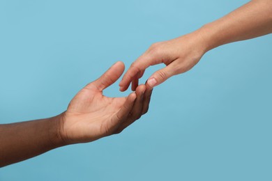 Photo of Woman and African American man touching hands on light blue background, closeup