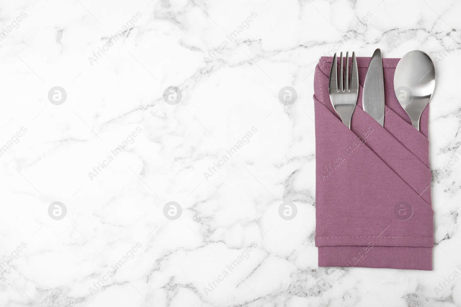 Photo of Folded napkin with fork, spoon and knife on marble background, top view. Space for text