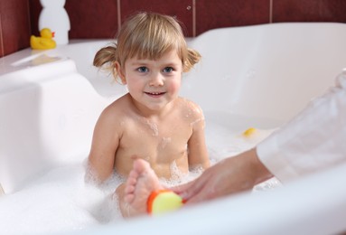 Photo of Mother washing her smiling daughter with sponge in bathtub, closeup