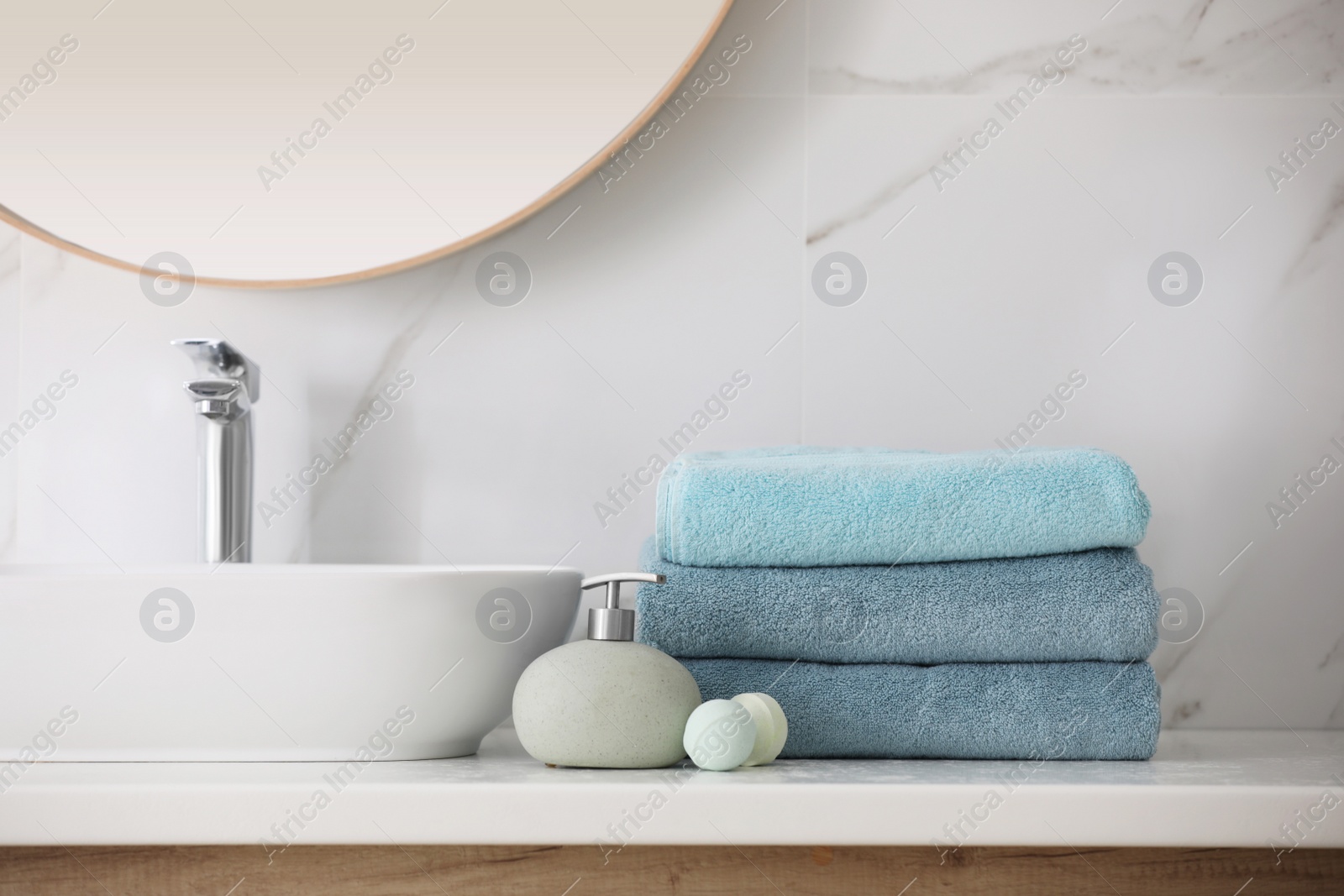 Photo of Stack of fresh towels, soap dispenser and bath bombs on countertop  indoors