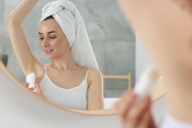 Beautiful woman applying deodorant near mirror in bathroom