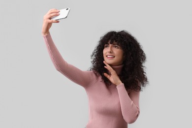 Photo of Beautiful young woman taking selfie on light grey background