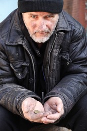 Poor homeless senior man holding coins outdoors