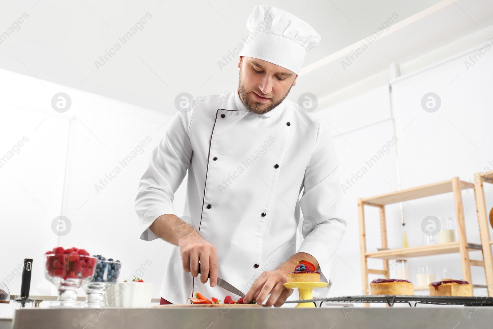 Photo of Male pastry chef cutting berries at table in kitchen