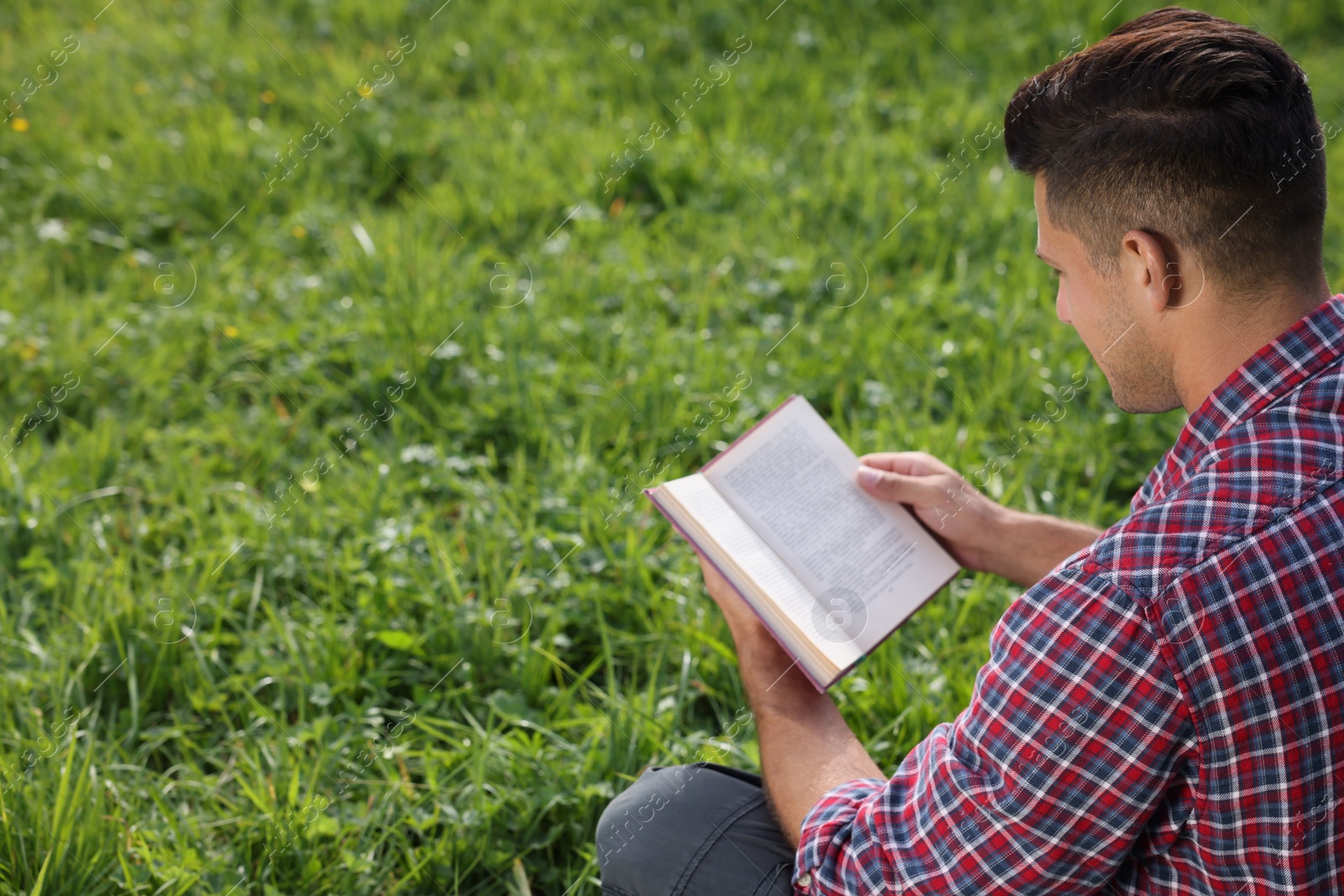 Photo of Man reading book on green grass outdoors